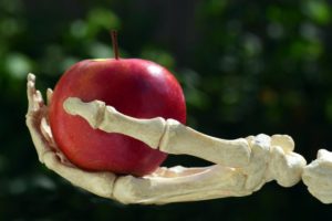 Une pommebien rouge tendue par une main squelettique