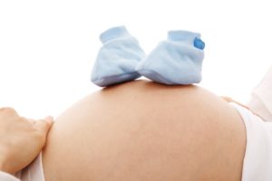 [Image d'illustration] Un ventre de personne enceinte avec des chaussons de bébé dessus