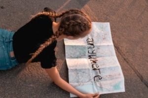 [Image d'illustration] Une jeune femme déploie un plan. En travers de ce dernier, il est écrit au feutre noir "Anywhere" ("quelque part")
